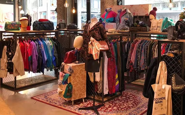 Vêtements rétro colorés suspendus sur un portant dans un marché vintage, symbolisant la revente de vêtements d’occasion.