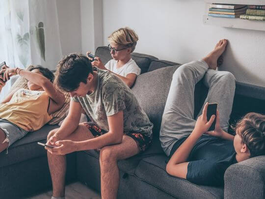 Quatre adolescents allongés sur un canapé, concentrés sur leurs téléphones portables, illustrant l’impact des influenceurs et des réseaux sociaux sur les jeunes